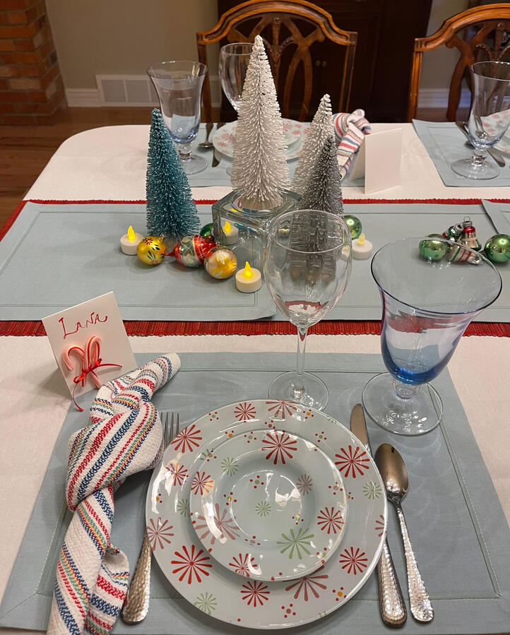Snowflake glass plates, vintage ornaments, and brushed bottle-brush trees create a winter table layered in blue glass and candlelight.